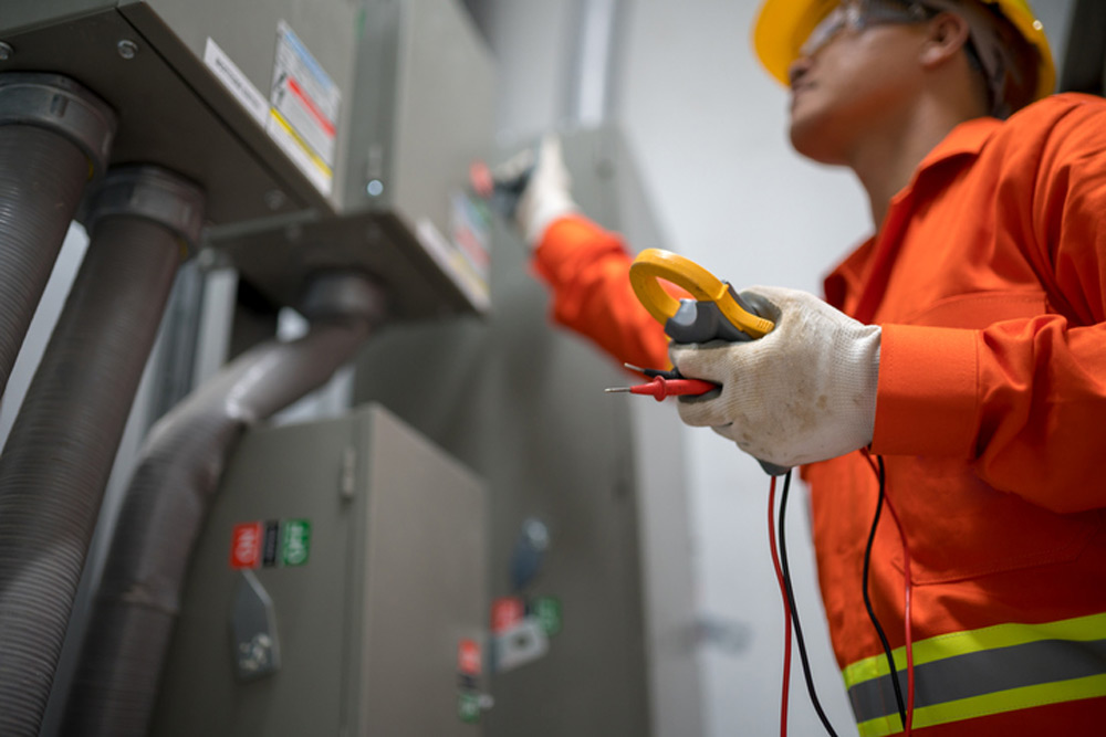 Elektriker i orange skyddskläder arbetar med kablar på byggarbetsplats